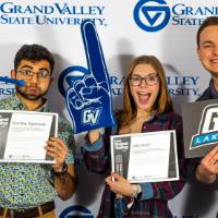 individuals smiling with horn, gvsu lakers sign, and foam finger